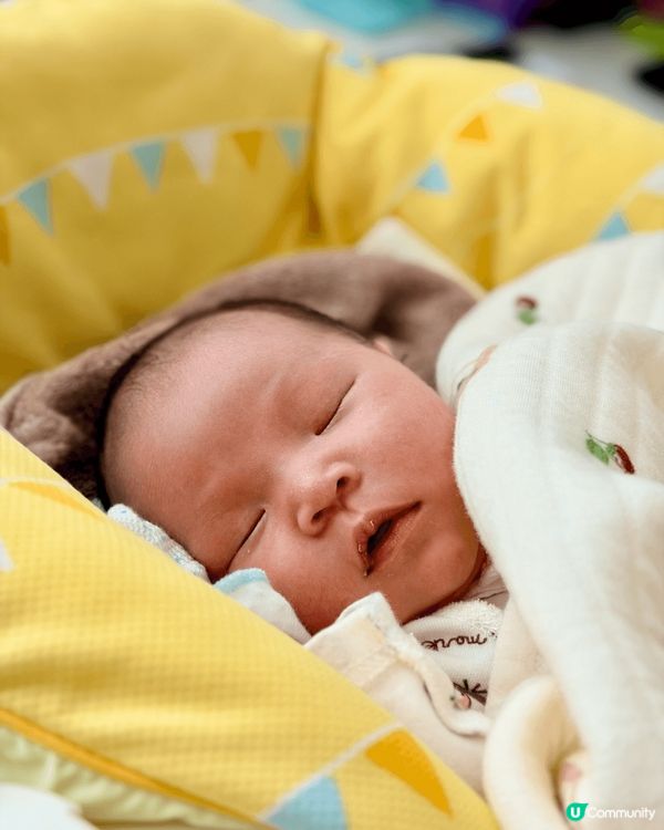 BB躺在柔軟的黃色嬰兒床中，雙手自然舉起，像是在伸展或開心地...