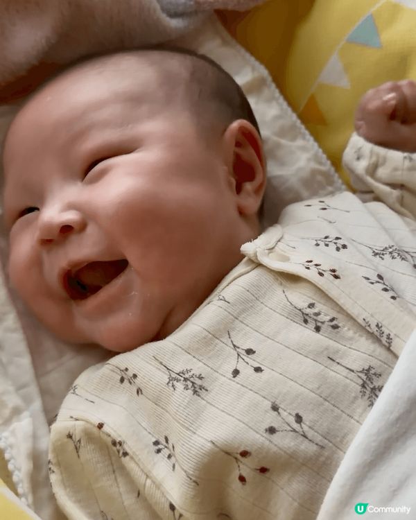 BB躺在柔軟的黃色嬰兒床中，雙手自然舉起，像是在伸展或開心地...