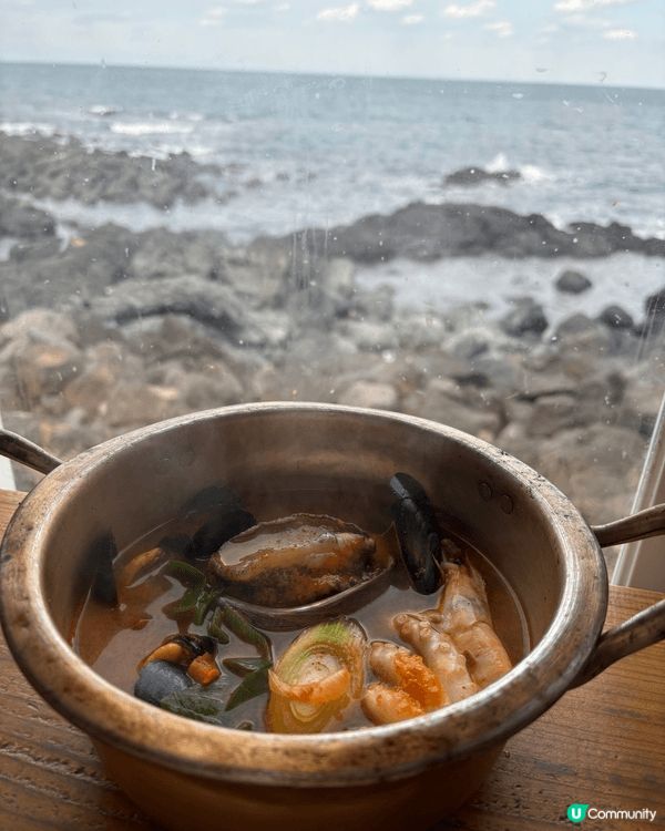 這是一碗豐盛的海鮮湯，裝在一個復古金屬鍋中，背景是海景。 湯...