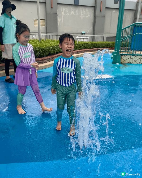 這張照片拍攝於戶外兒童水上樂園，兩位小朋友在噴水池之中開心玩...